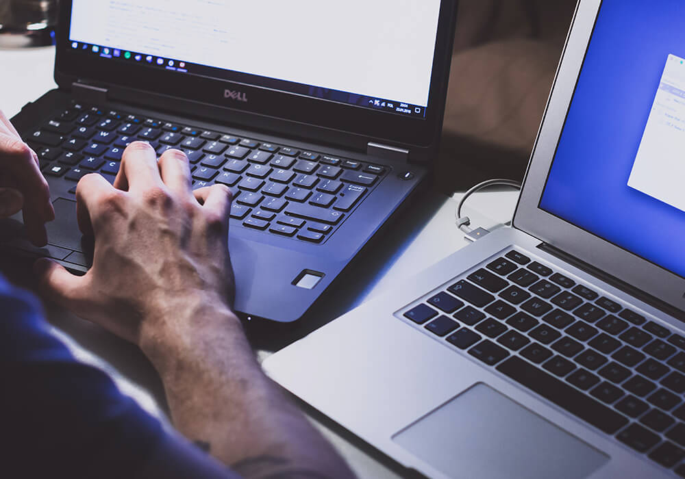 image of an IT tech working on two laptops