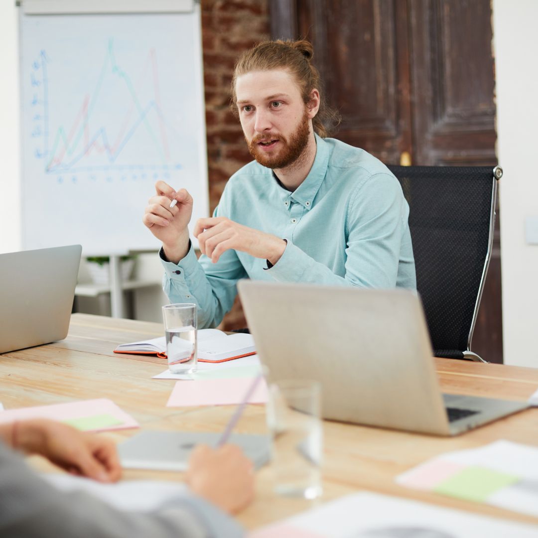 a man talking in a meeting in front of a laptop